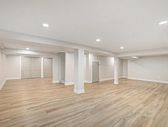 Finished basement in Philadelphia with wide plank laminate flooring, recessed lighting, neutral walls, and double doors to storage.