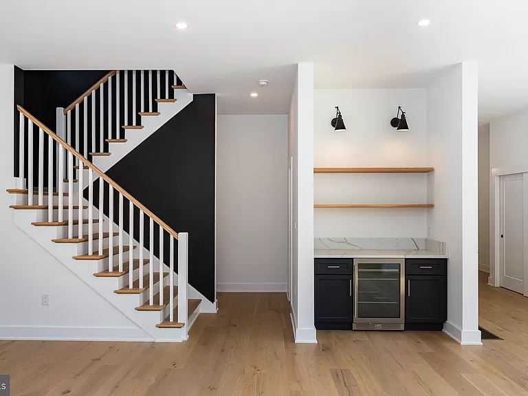 Transitional interior space with light wood flooring, black staircase accent wall, and finished basement style bar area with black cabinetry and marble countertops.